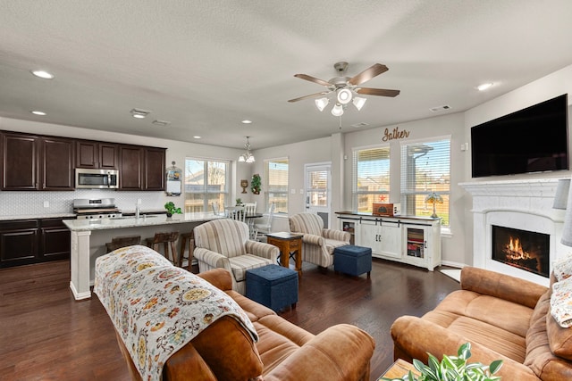 living room with recessed lighting, dark wood-style flooring, visible vents, and a lit fireplace