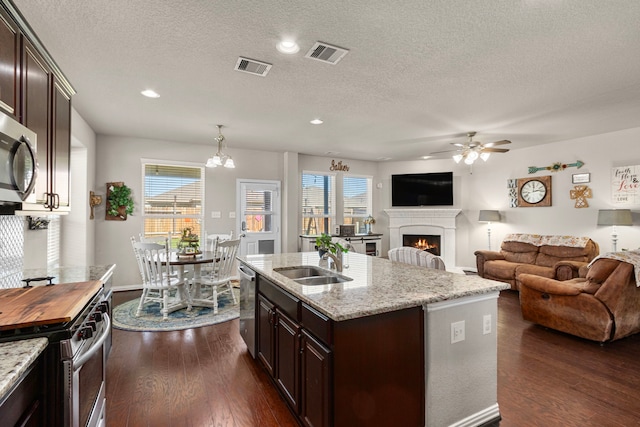 kitchen with dark wood-style flooring, stainless steel appliances, visible vents, a sink, and a lit fireplace