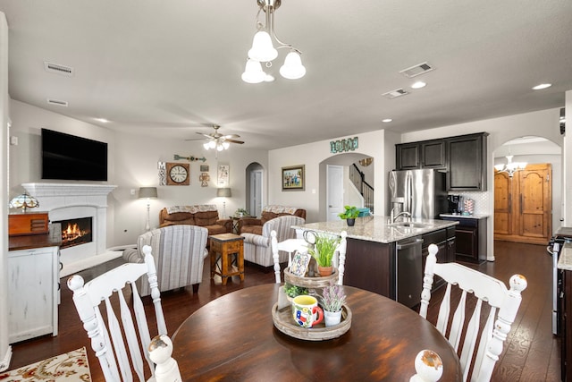 dining room featuring arched walkways, a warm lit fireplace, visible vents, and ceiling fan with notable chandelier