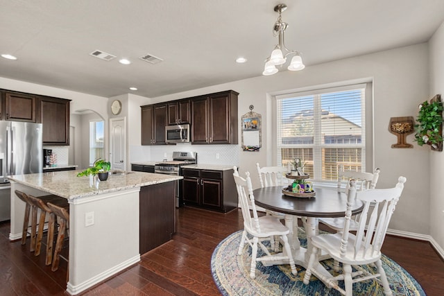 kitchen featuring a center island with sink, arched walkways, stainless steel appliances, and dark wood finished floors