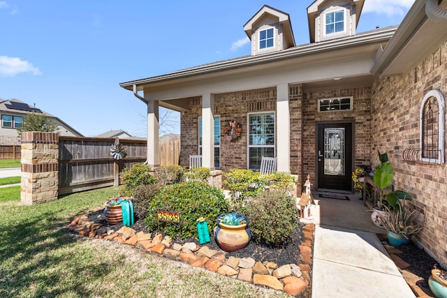 entrance to property featuring fence, a porch, a lawn, and brick siding