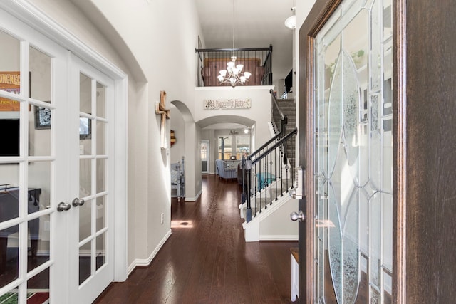 entryway with arched walkways, wood finished floors, an inviting chandelier, stairs, and french doors