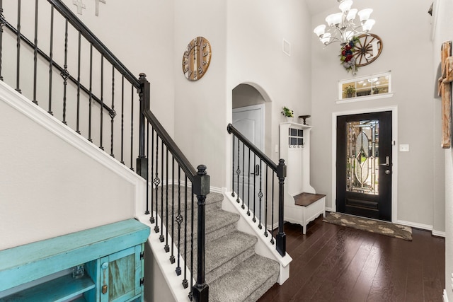 foyer entrance with arched walkways, a notable chandelier, wood-type flooring, a high ceiling, and baseboards