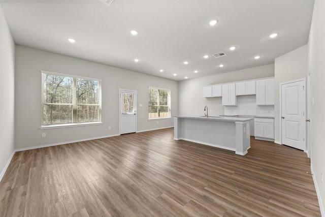 kitchen featuring visible vents, an island with sink, wood finished floors, white cabinetry, and a sink