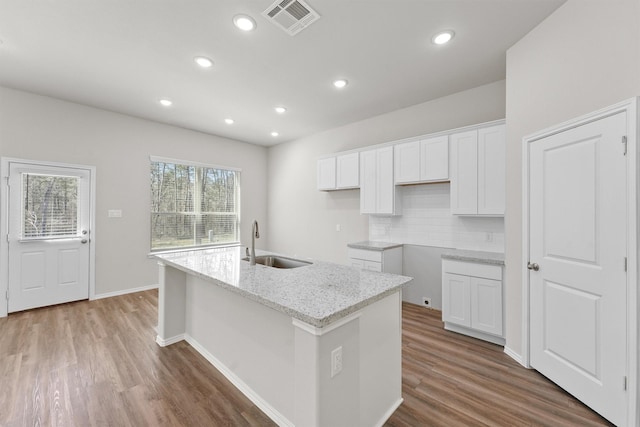 kitchen with visible vents, a kitchen island with sink, a sink, white cabinetry, and wood finished floors