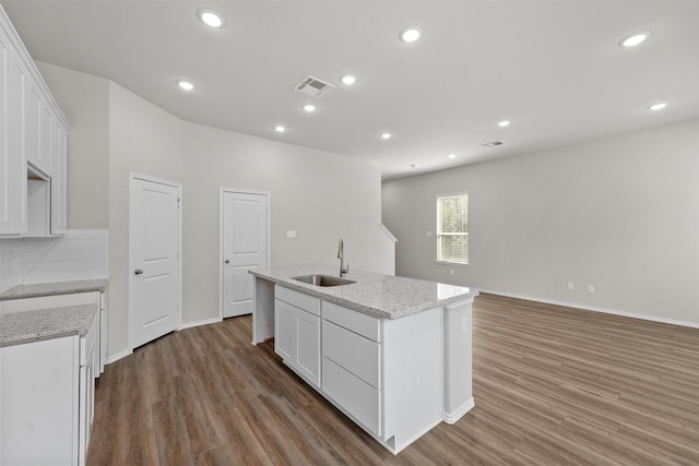 kitchen with wood finished floors, an island with sink, a sink, and backsplash