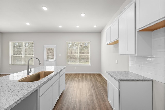 kitchen with light wood finished floors, light stone counters, white cabinets, and a sink