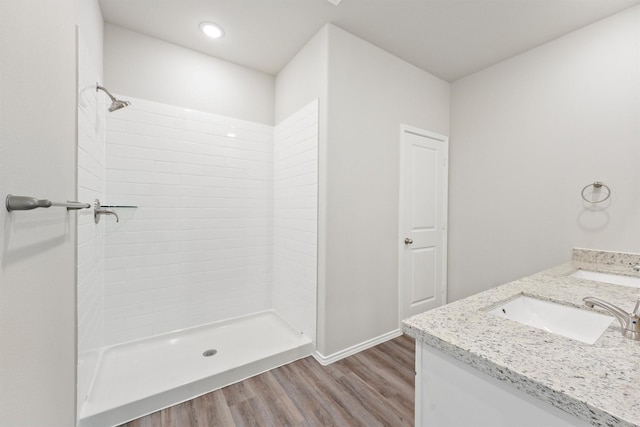 bathroom featuring double vanity, tiled shower, a sink, and wood finished floors