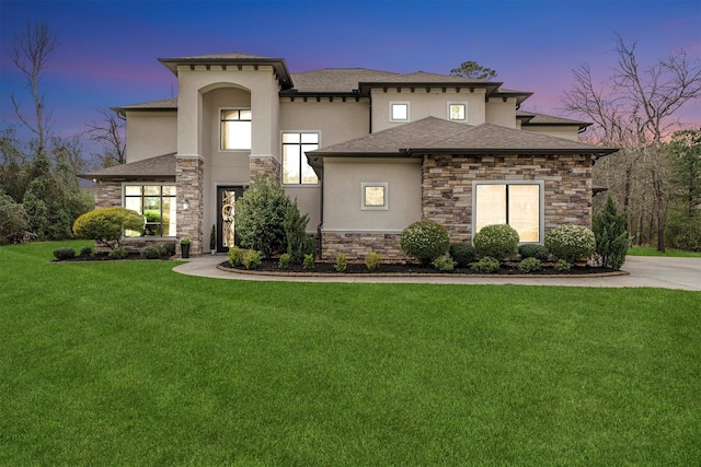 view of front of house with a shingled roof, stone siding, a lawn, and stucco siding