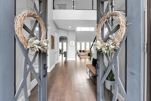 foyer entrance with baseboards, a high ceiling, arched walkways, and dark wood-type flooring