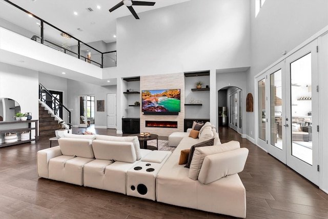 living room featuring arched walkways, dark wood finished floors, a warm lit fireplace, baseboards, and stairs