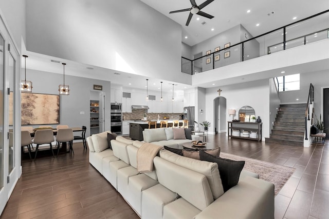 living room featuring arched walkways, dark wood-style flooring, visible vents, stairway, and ceiling fan with notable chandelier