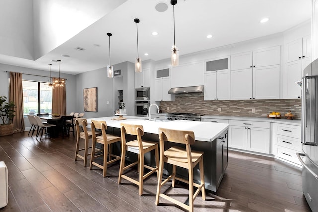 kitchen featuring appliances with stainless steel finishes, dark wood-style flooring, light countertops, under cabinet range hood, and backsplash