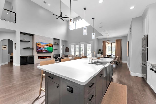 kitchen featuring arched walkways, a ceiling fan, a spacious island, dark wood-type flooring, and a lit fireplace