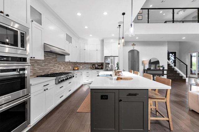 kitchen featuring arched walkways, under cabinet range hood, stainless steel appliances, white cabinetry, and a kitchen bar