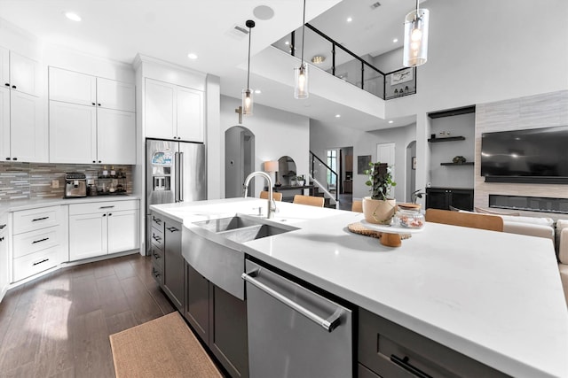 kitchen featuring arched walkways, stainless steel appliances, open floor plan, light countertops, and decorative backsplash