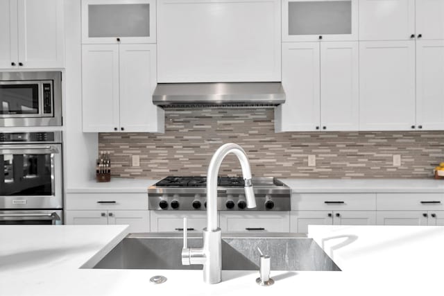 kitchen with appliances with stainless steel finishes, backsplash, exhaust hood, and white cabinets