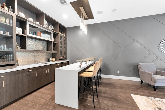 bar featuring visible vents, decorative backsplash, wet bar, wood finish floors, and a sink