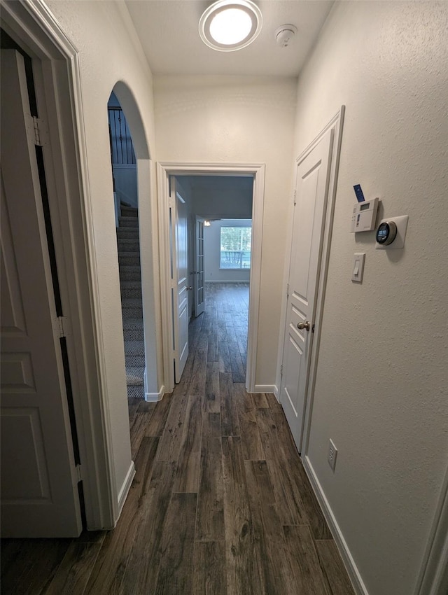 corridor with dark wood-style floors, stairway, arched walkways, and baseboards