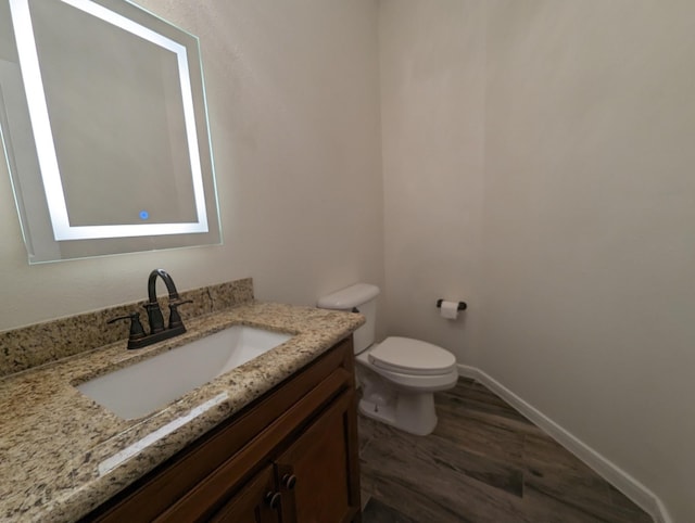 bathroom with toilet, baseboards, wood finished floors, and vanity