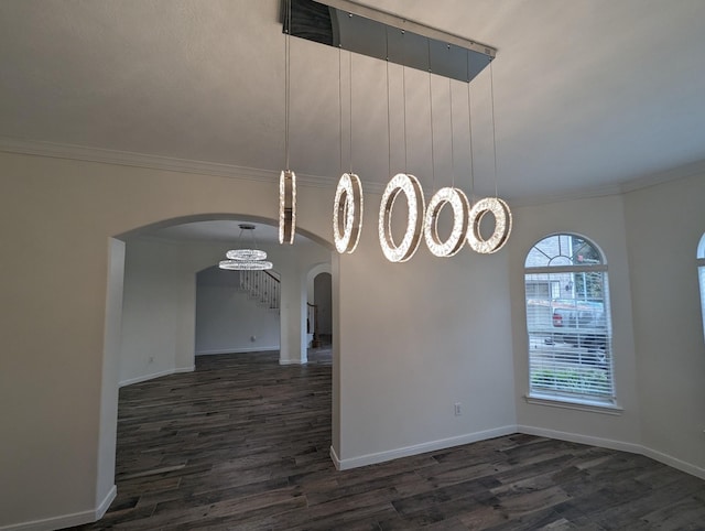 spare room featuring arched walkways, baseboards, stairway, dark wood-type flooring, and crown molding