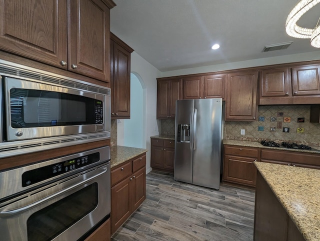 kitchen with light stone counters, visible vents, backsplash, appliances with stainless steel finishes, and light wood-type flooring