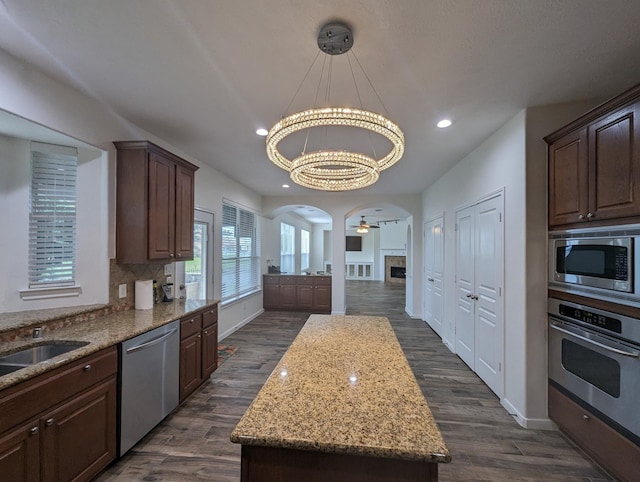 kitchen with light stone counters, arched walkways, dark wood-style floors, stainless steel appliances, and decorative backsplash