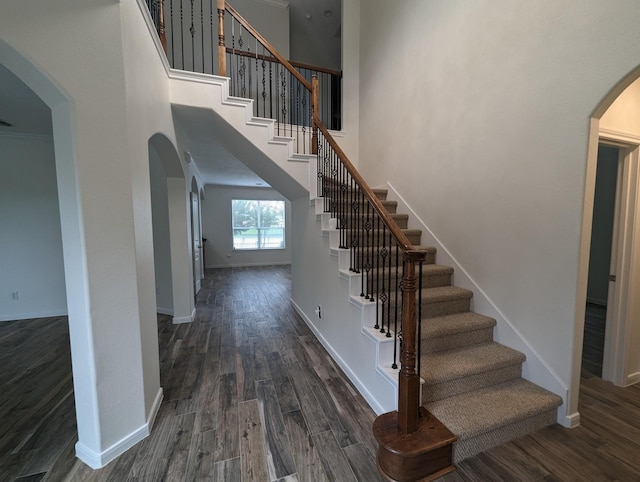 staircase with arched walkways, a high ceiling, wood finished floors, and baseboards