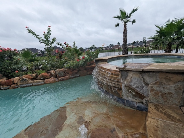 view of pool with fence and a pool with connected hot tub