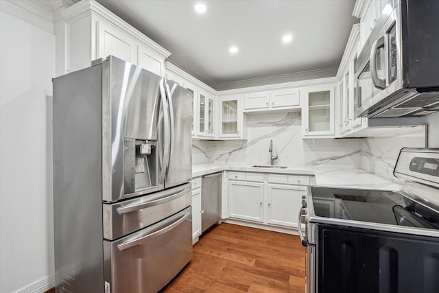 kitchen with decorative backsplash, appliances with stainless steel finishes, light wood-style floors, white cabinetry, and light stone countertops