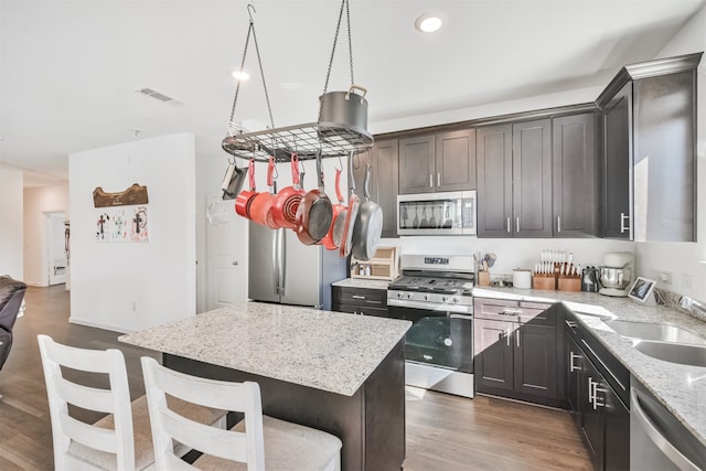 kitchen with stainless steel appliances, wood finished floors, a sink, visible vents, and light stone countertops