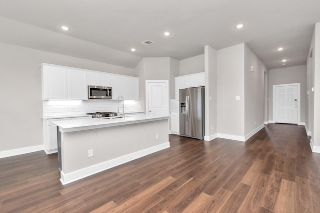 kitchen featuring tasteful backsplash, a center island with sink, visible vents, dark wood-style floors, and stainless steel appliances