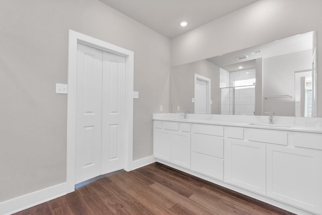 bathroom with double vanity, a sink, a shower stall, wood finished floors, and baseboards