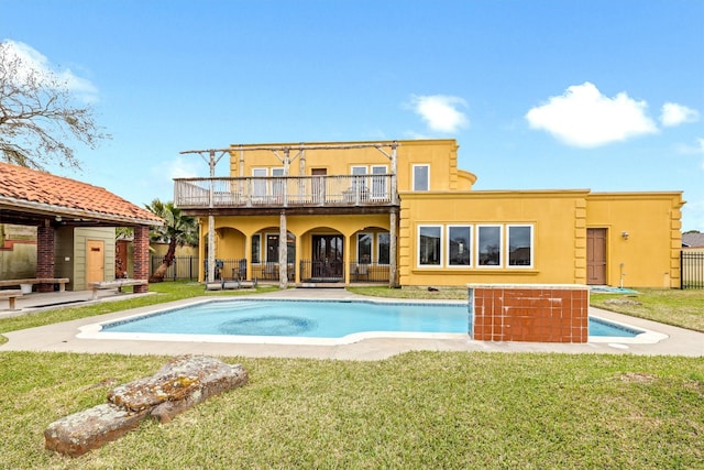 rear view of property featuring a yard, an outdoor pool, fence, and stucco siding