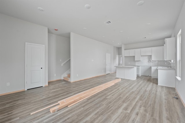 unfurnished living room with light wood-type flooring, baseboards, stairs, and visible vents