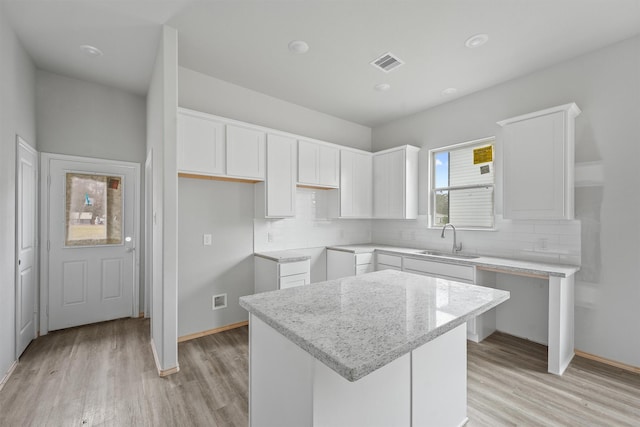 kitchen with white cabinetry, a sink, light wood-style flooring, and decorative backsplash