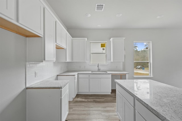 kitchen with light stone counters, a sink, visible vents, light wood-type flooring, and tasteful backsplash