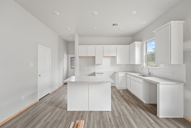 kitchen with light wood-style floors, a center island, a sink, and tasteful backsplash