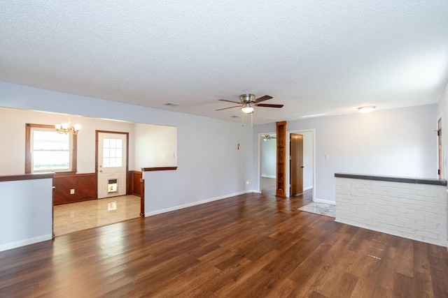 unfurnished living room with ceiling fan with notable chandelier, visible vents, a textured ceiling, and wood finished floors