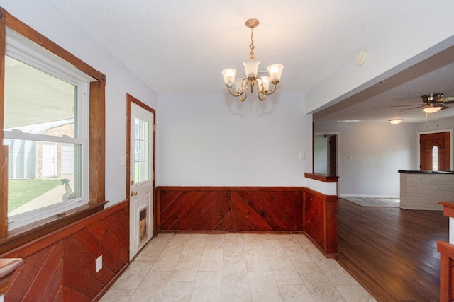 spare room featuring a wainscoted wall, wooden walls, a textured ceiling, and ceiling fan with notable chandelier