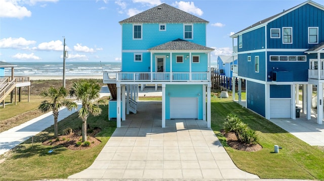 beach home featuring a shingled roof, an attached garage, a water view, a front lawn, and a carport