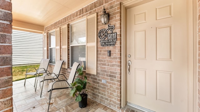 view of exterior entry featuring covered porch and brick siding