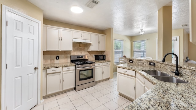 kitchen featuring gas range, a sink, under cabinet range hood, black microwave, and backsplash