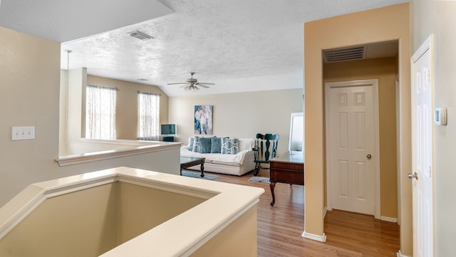 hallway with light wood-style floors, visible vents, a textured ceiling, and an upstairs landing