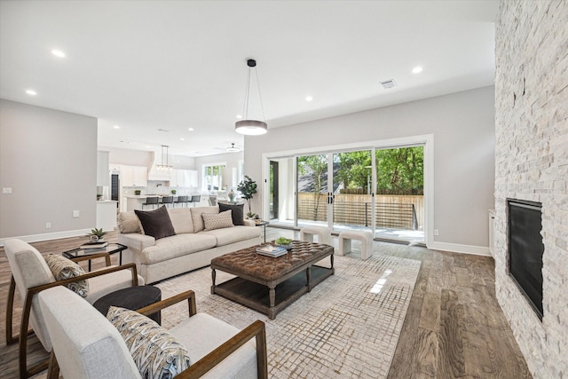 living area with recessed lighting, baseboards, wood finished floors, and a stone fireplace