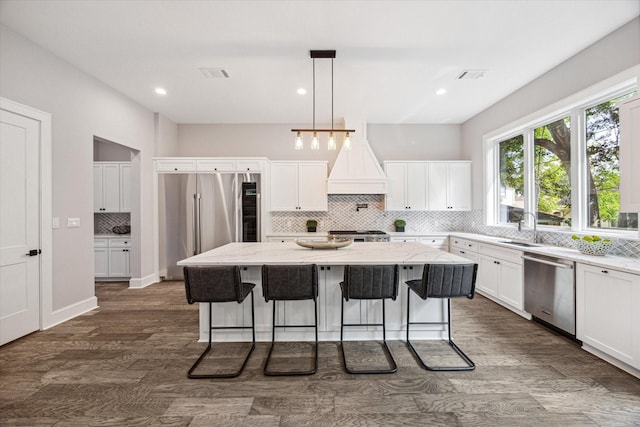 kitchen with dark wood-style flooring, a kitchen island, white cabinets, appliances with stainless steel finishes, and custom range hood