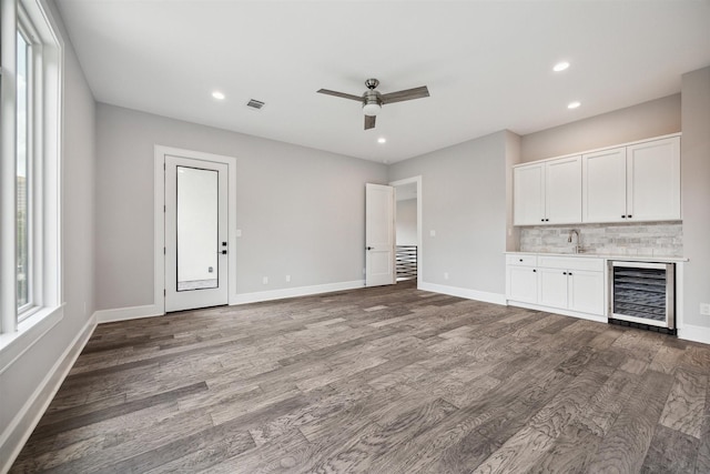 unfurnished living room featuring visible vents, a sink, wood finished floors, beverage cooler, and baseboards