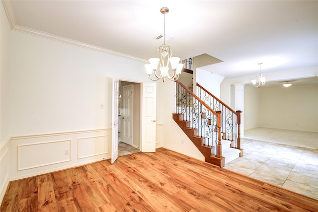 empty room featuring light wood-type flooring, ornate columns, stairs, and a notable chandelier