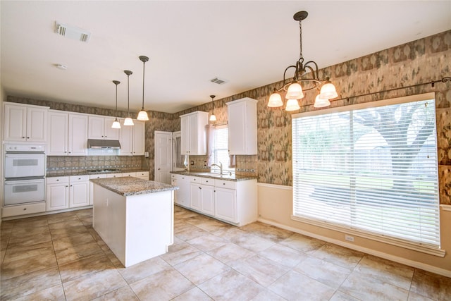 kitchen featuring under cabinet range hood, gas stovetop, white cabinetry, visible vents, and wallpapered walls