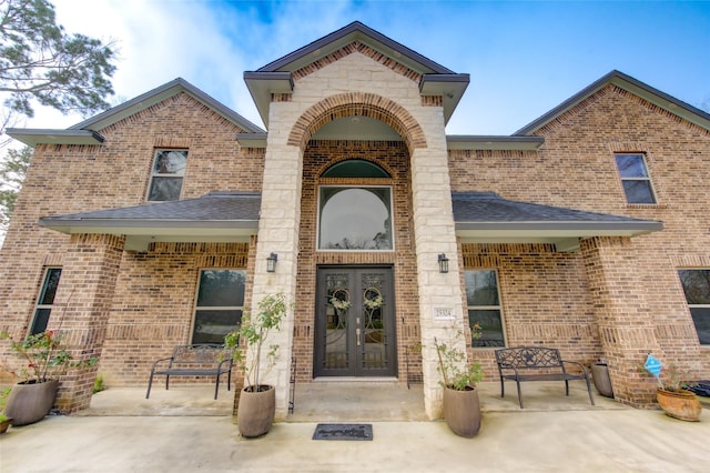 doorway to property with brick siding, roof with shingles, stone siding, and french doors